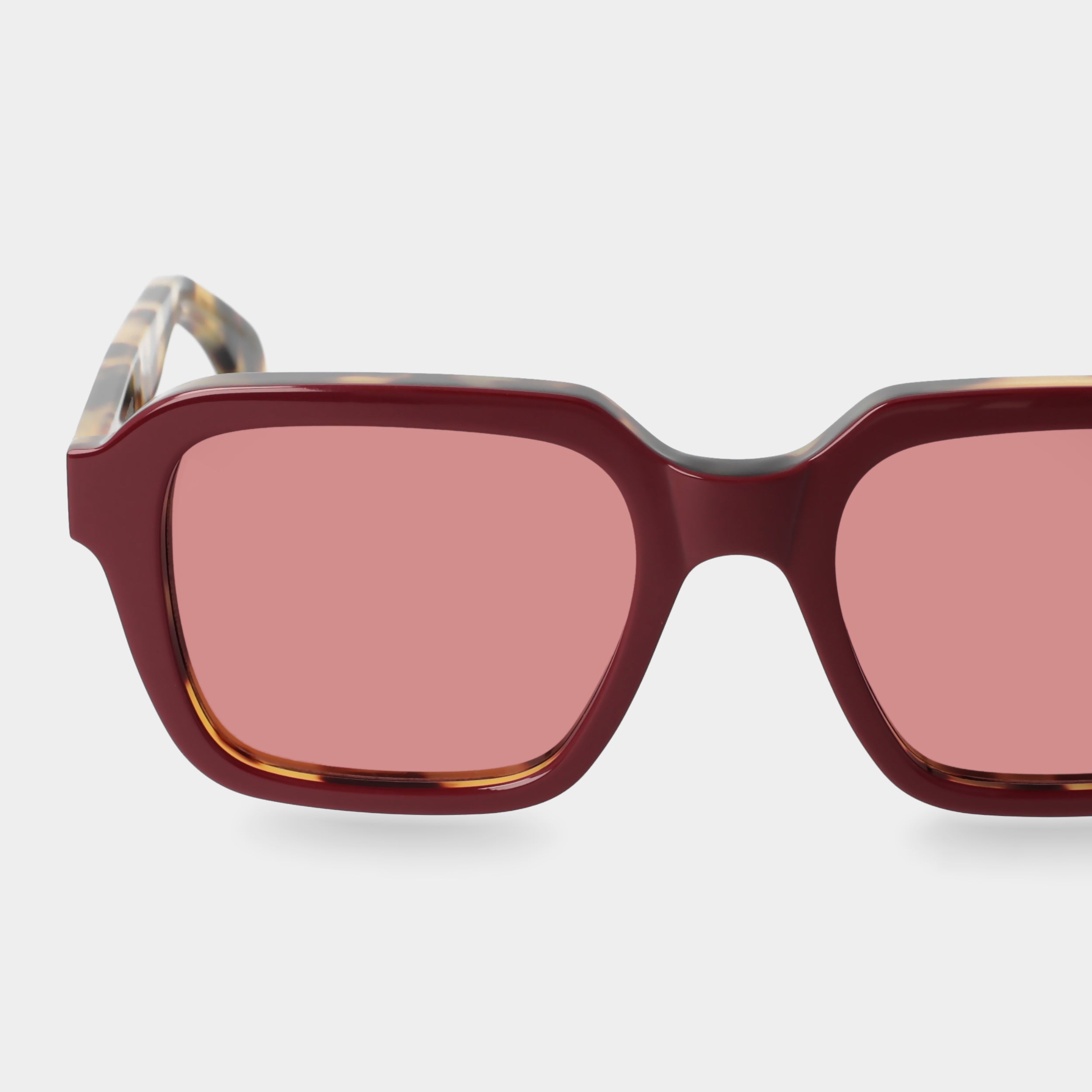 Sunglasses with red-tinted lenses on a light gray background. - Dei Duchi