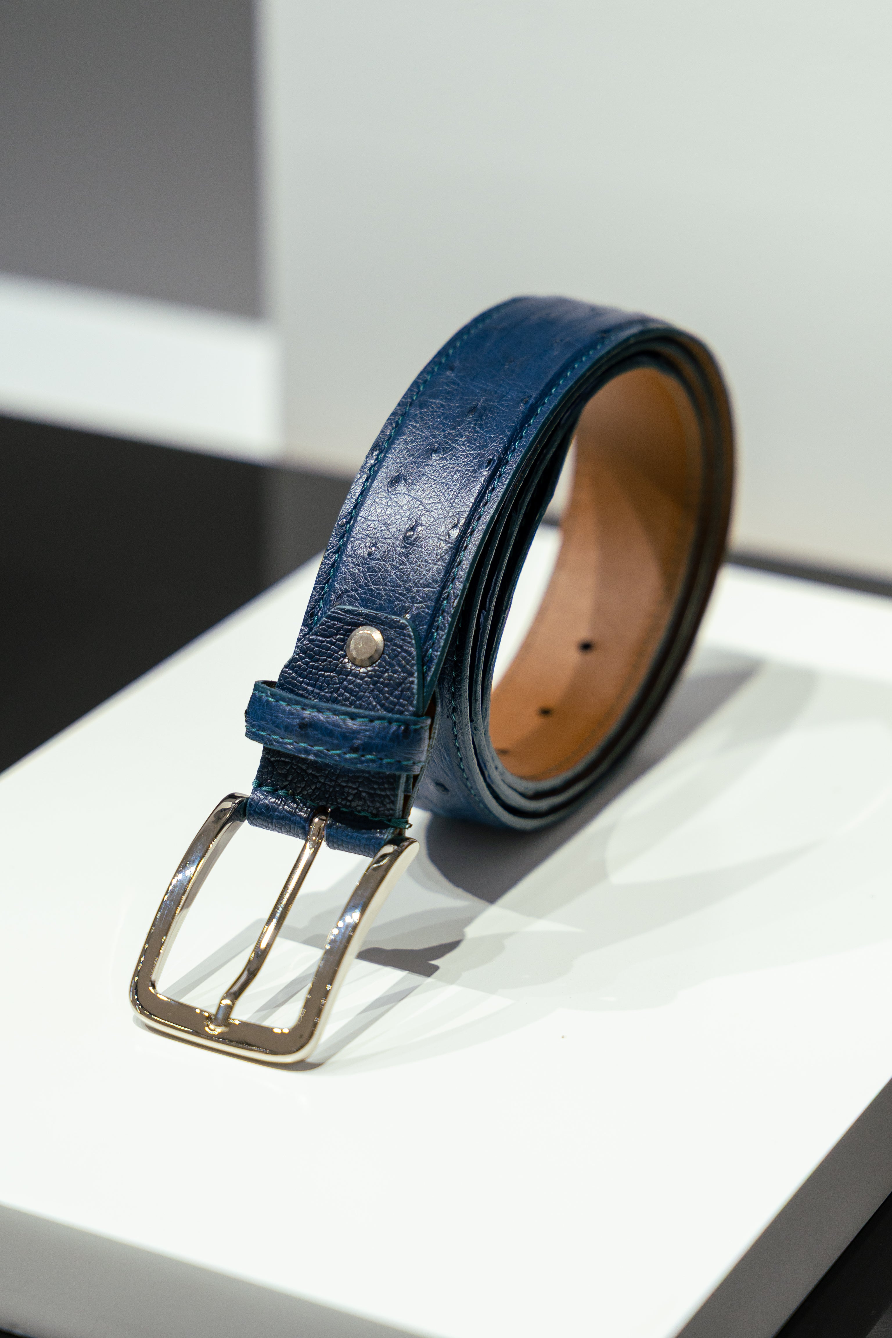 Blue leather belt with a gold buckle on a white surface. - Sartoria Dei Duchi-Atri