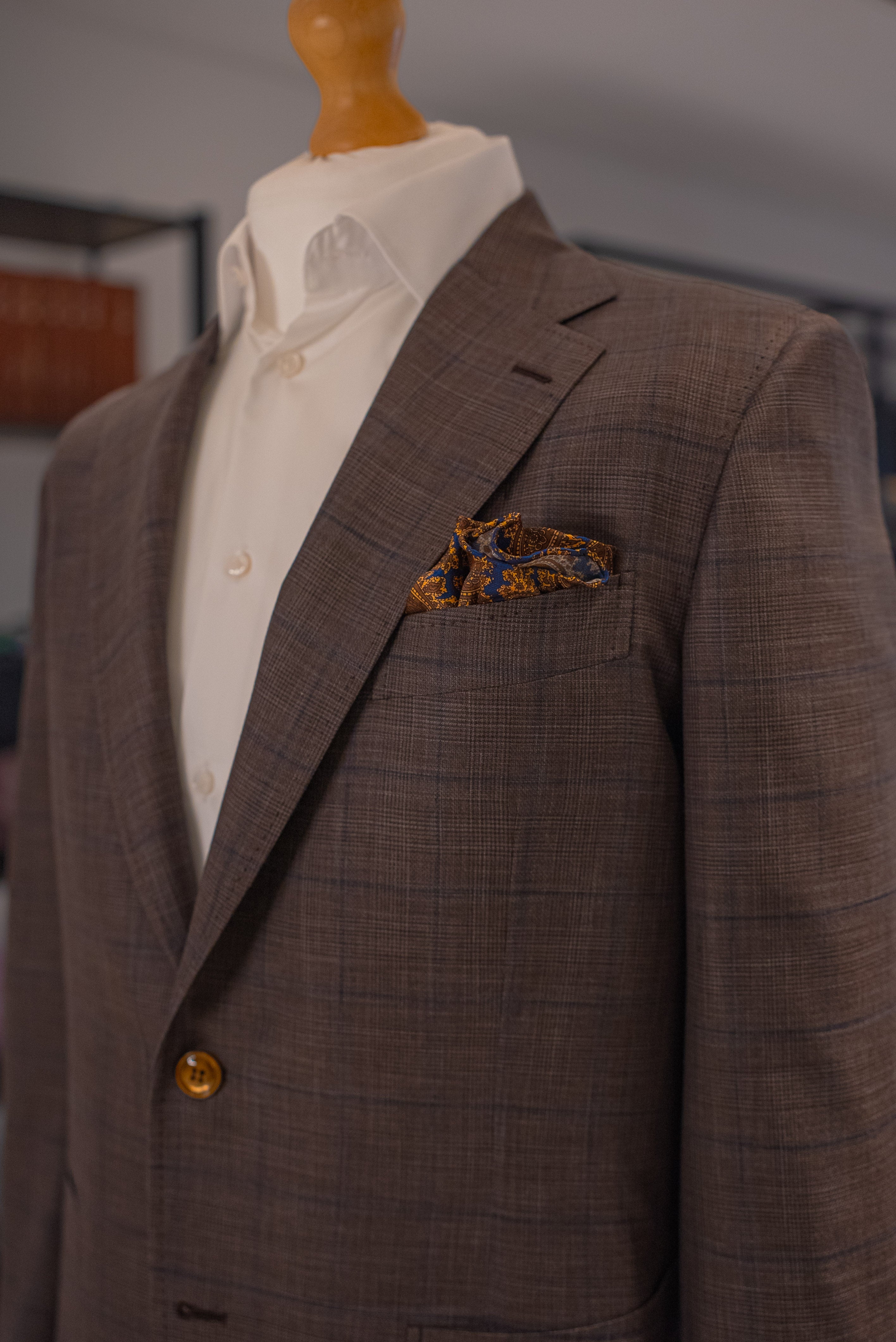 Brown suit jacket on a mannequin with a white shirt and patterned pocket square. - Sartoria Dei Duchi-Atri