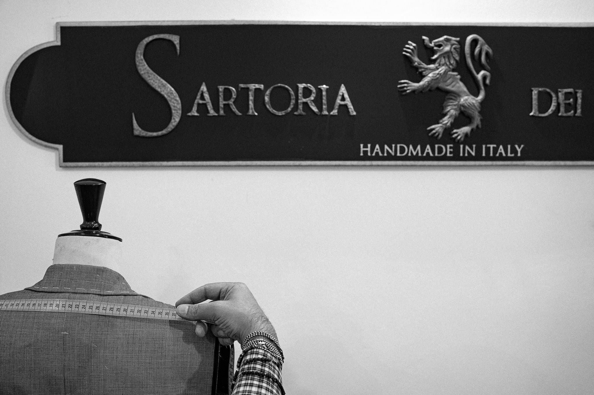 Person adjusting a garment on a mannequin in front of a 'Sartoria Dei' sign.