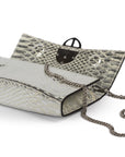 Laid view of a silvery snake textured leather bag with a 'AMALTEA' burnished metal buckle logo, and a silver chain strap, on a white background. - DEI DUCHI (AMALTEA)