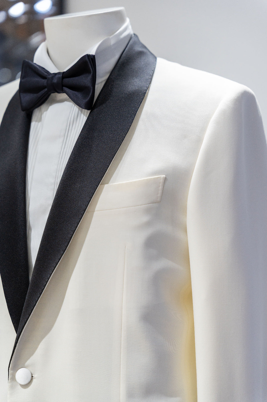 White tuxedo jacket with black lapels and bow tie on a mannequin against a gray background. - Sartoria Dei Duchi-Atri