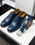 Blue dress shoes with a matching belt on a white surface. - Sartoria Dei Duchi-Atri