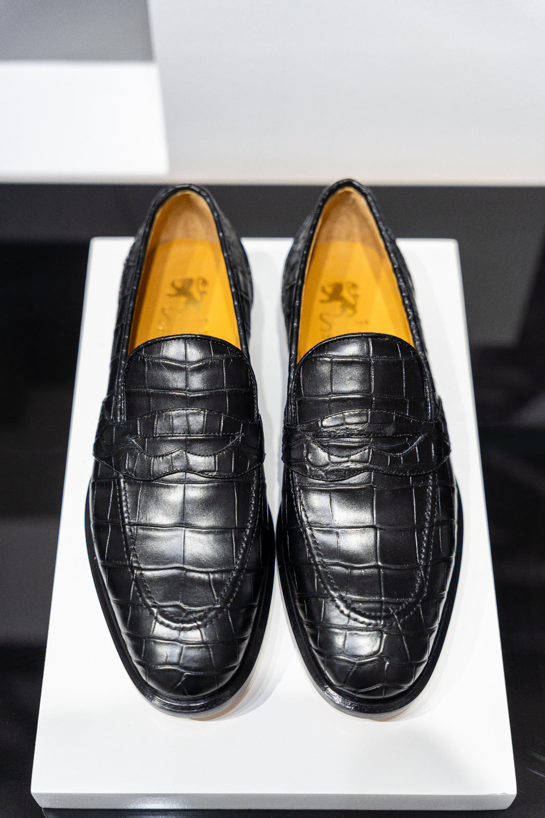 Pair of black crocodile-textured loafers on a white platform. - DEI DUCHI