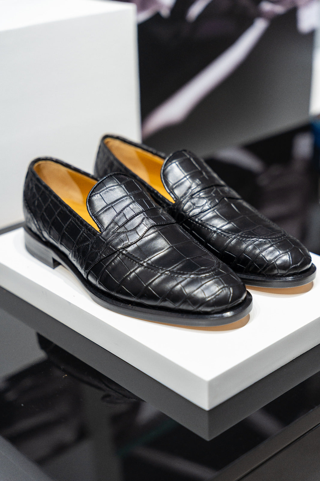 Pair of black crocodile-textured loafers on a white platform. - DEI DUCHI