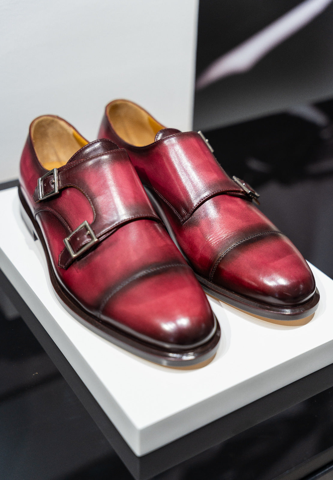 Pair of red leather shoes with brown soles on a white platform. - Sartoria Dei Duchi