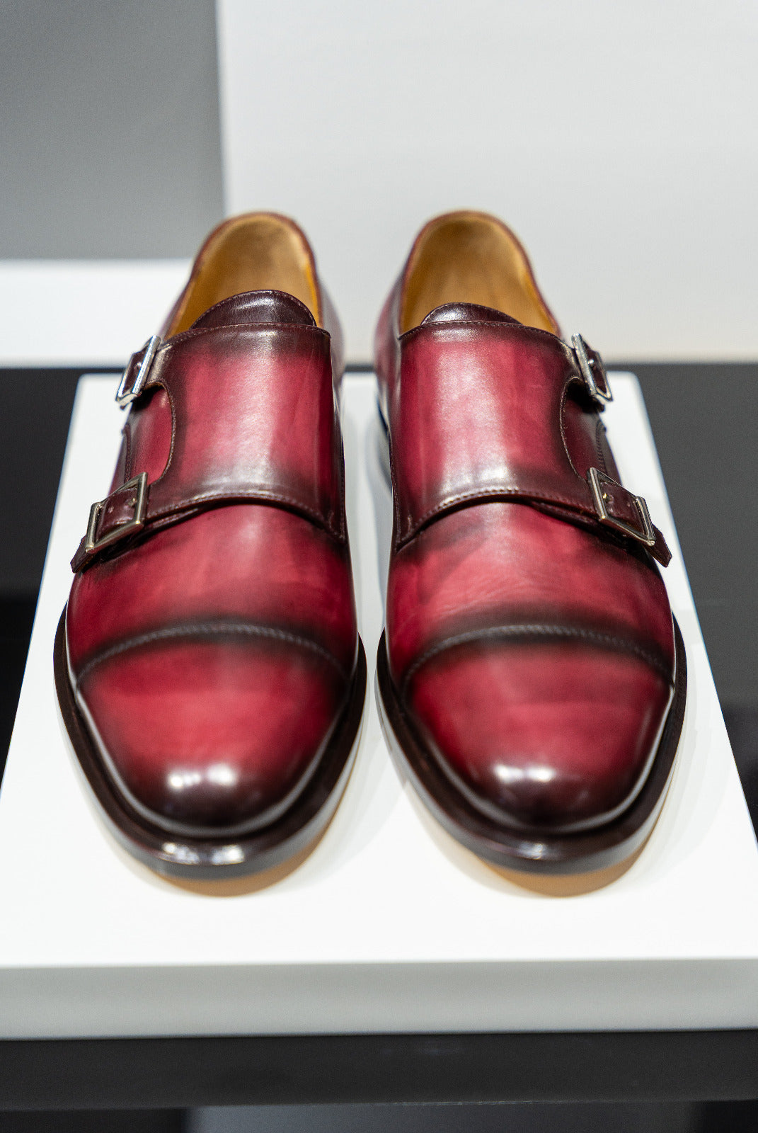 Pair of red leather shoes with brown soles on a white platform. - Sartoria Dei Duchi