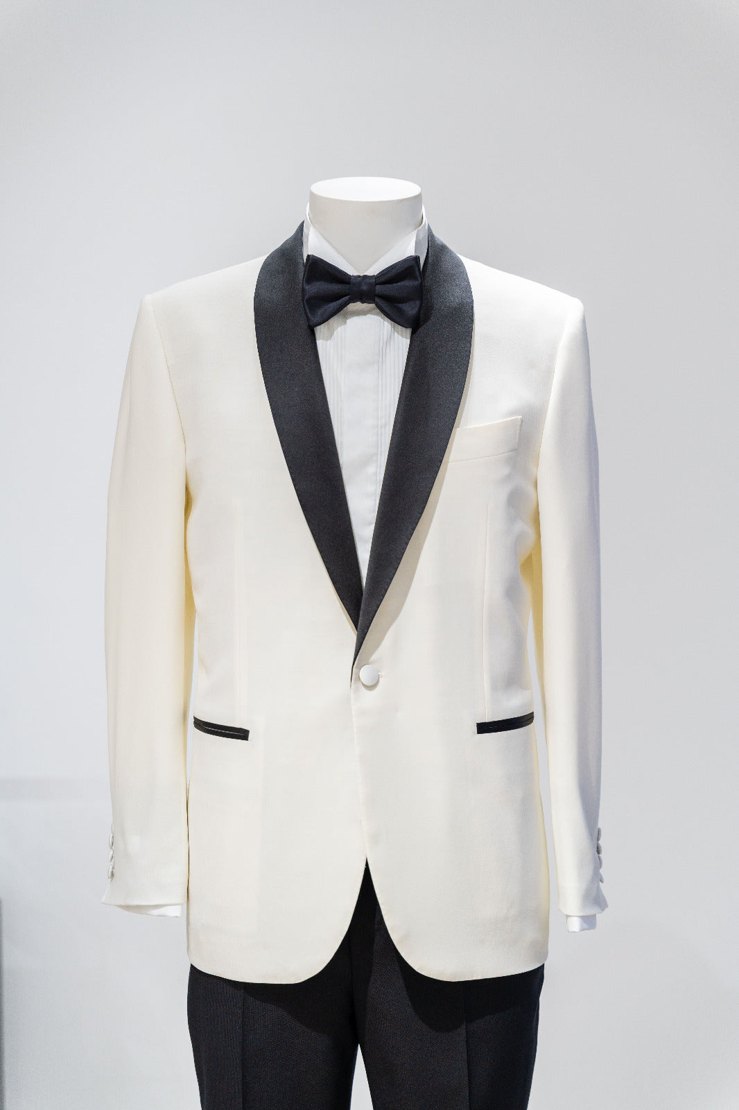 White tuxedo jacket with black lapels and bow tie on a mannequin against a gray background. - Sartoria Dei Duchi-Atri