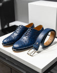 Blue dress shoes with a matching belt on a white platform. - Blue leather belt with a gold buckle on a white surface. - Sartoria Dei Duchi-Atri
