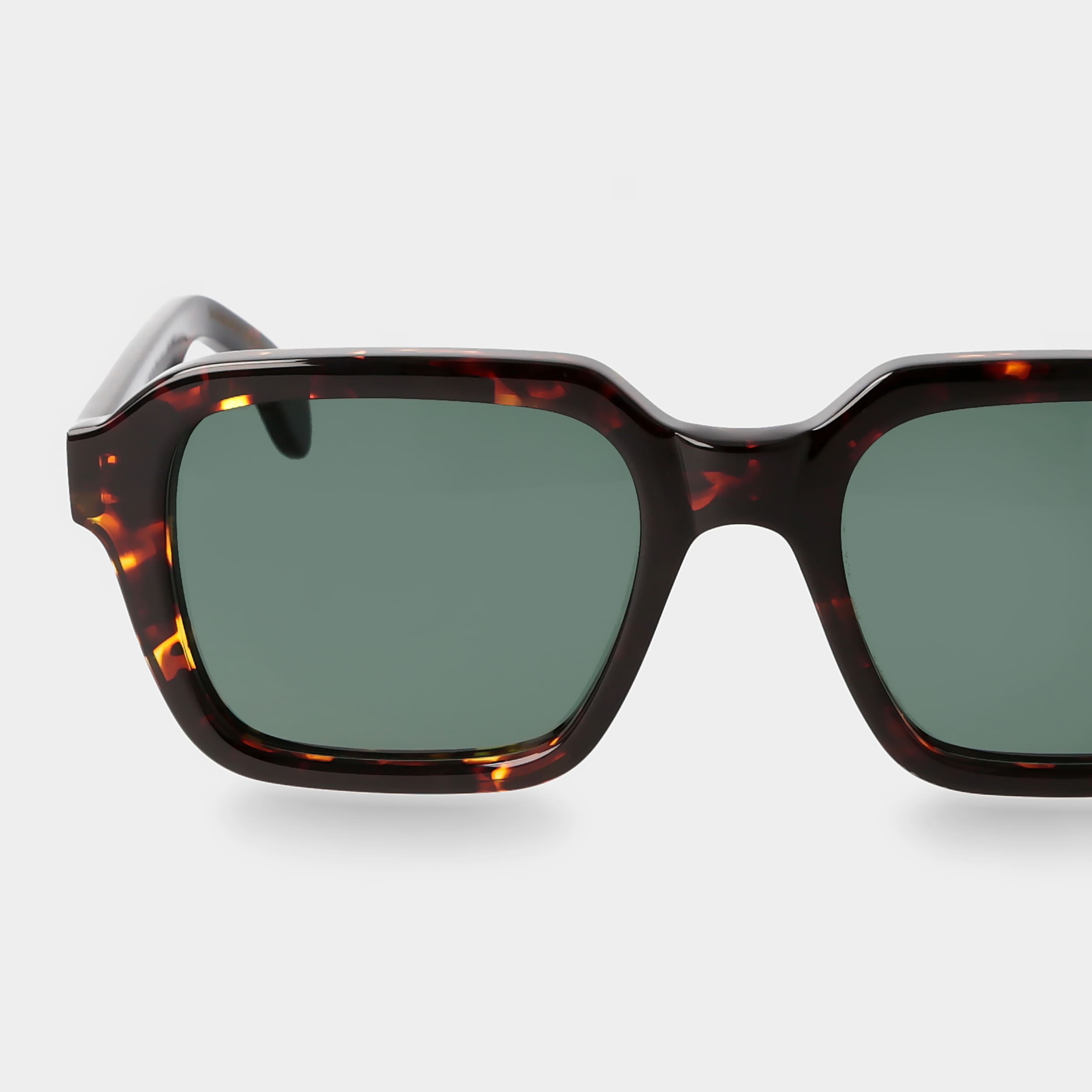 Sunglasses with tortoiseshell frame and green lenses on a light gray background. _ DEI DUCHI
