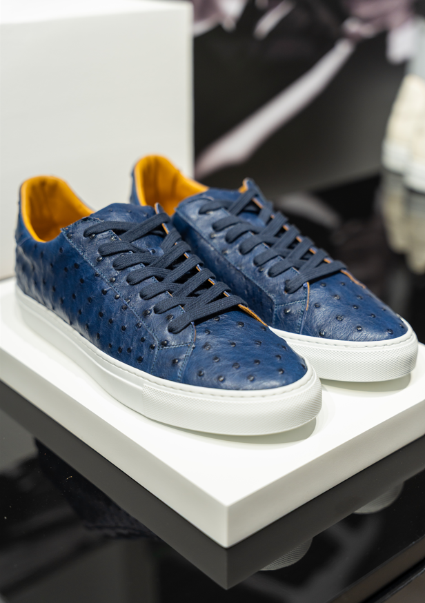A pair of navy blue ostrich leather sneakers with white soles displayed on a platform. - Sartoria Dei Duchi-Atri