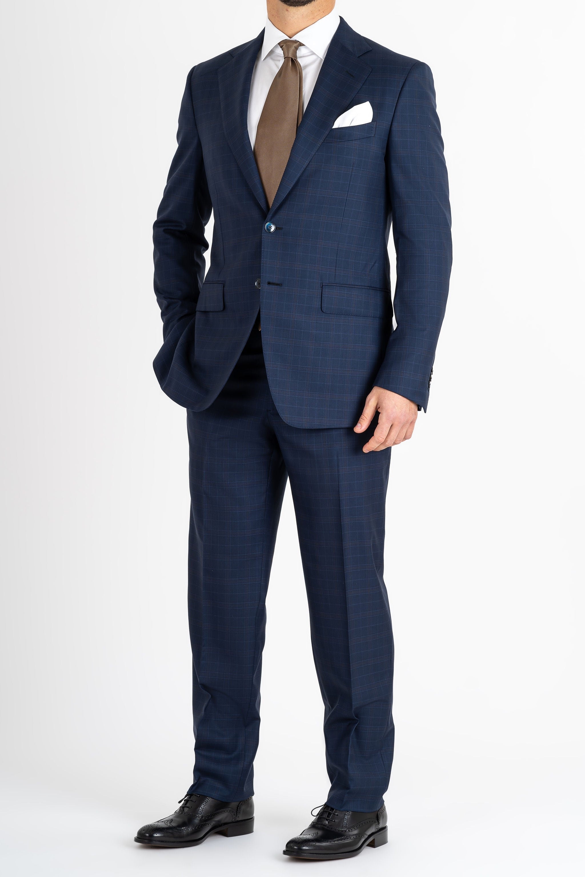 This Sartoria dei Duchi suit is made with a Caccioppoli 150s fabric made with 96% wool and 4% of Cashmere. The fabric has a midnight blue and light brown checked pattern. The jacket is fully lined and is made with two buttons, flap pockets and classic lapel. Pants are made without pleats, with American style pockets and comfortable no- slip belt loops. Side stitching on jacket and trousers.