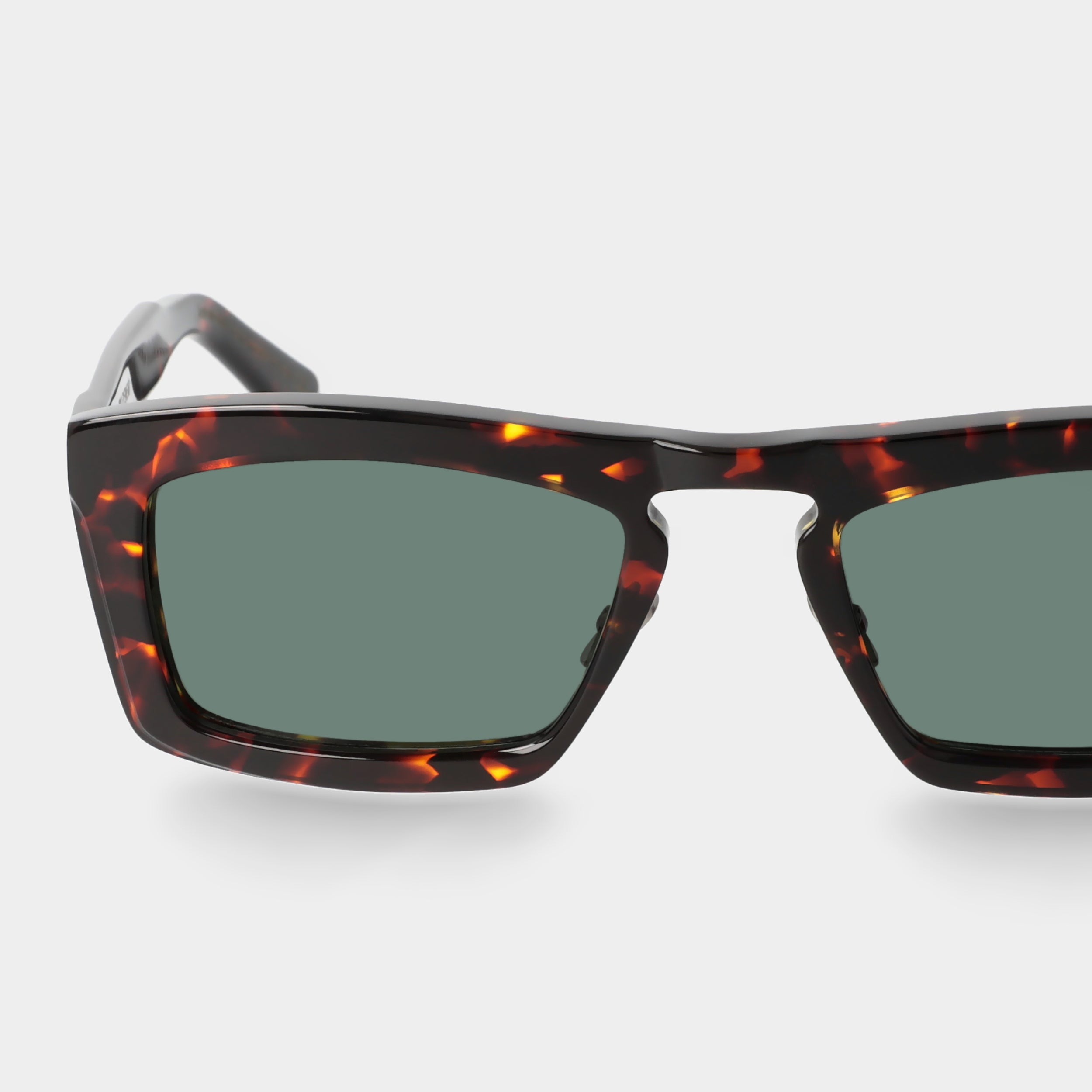 Sunglasses with tortoiseshell frame and green lenses on a light gray background. - De Duchi
